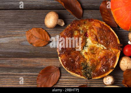 Crostate di pollo, funghi, spinaci e pomodori con foglie autunnali su sfondo rustico di legno. vista dall'alto Foto Stock