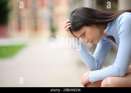 Profilo di una donna triste che si lamenta da sola in una strada Foto Stock