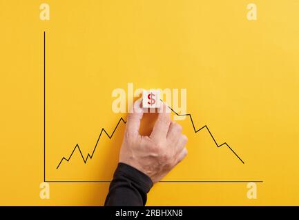 Prevedere la fluttuazione del mercato in valuta in dollari. La mano tiene il cubo di legno con il simbolo del dollaro con un grafico crescente e decrescente. Foto Stock