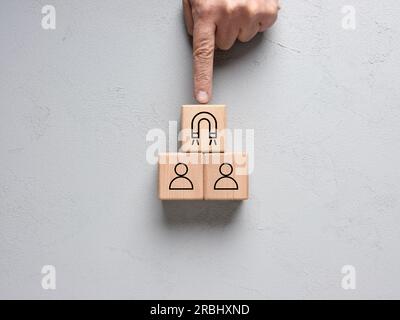 Attrazione o acquisizione da parte del cliente. Generazione di lead aziendali. Strategia di fidelizzazione dei clienti. La mano maschile mette un cubo di legno con il simbolo del magnete sul cubo Foto Stock