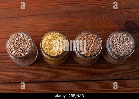 Grani di cereali in vasetti di vetro su fondo di legno. Collezione di diverse semole vista dall'alto orzo, avena, miglio e frumento. Alimenti integrali con alta f Foto Stock