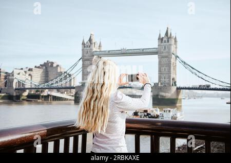 Donna bionda dai capelli lunghi che fotografa Tower Bridge Foto Stock