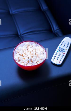 Ciotola di popcorn sul divano nero la sera Foto Stock