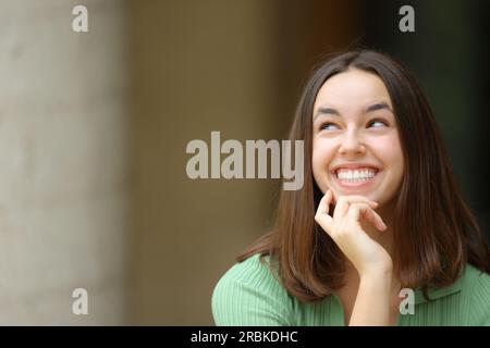 Vista frontale di una donna felice che guarda lateralmente che si chiede in strada Foto Stock