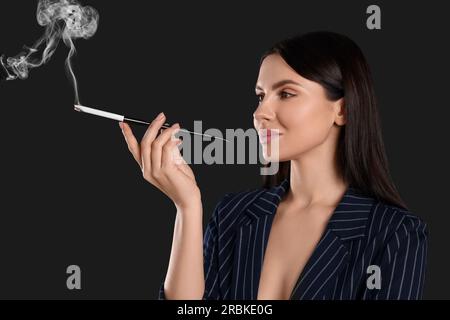 Donna che usa un portabicchieri lungo per fumare su sfondo nero Foto Stock
