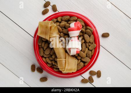 Cibo secco per cani e dolcetti (masticare le ossa) su pavimento di legno bianco, piatto Foto Stock