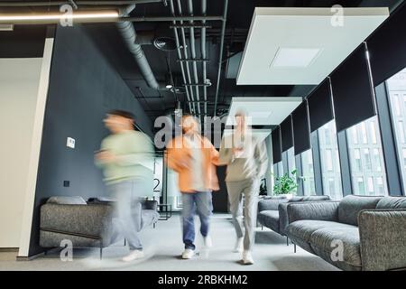 sfocatura del movimento degli imprenditori moderni in abiti informali che camminano lungo il corridoio della lounge con comodi divani in un ufficio di coworking con interi high-tech Foto Stock