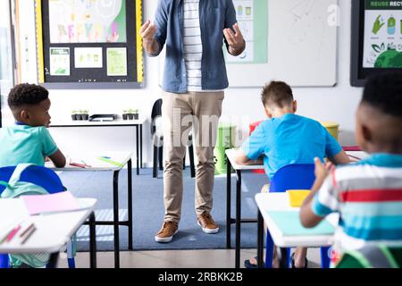 Sezione bassa di insegnanti maschi e diversi alunni alle scrivanie della scuola elementare, spazio per le copie. Istruzione, inclusività, scuola elementare e lear Foto Stock