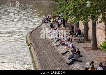 La gente al tramonto si siede sulla riva del fiume Senna sull'Ile de Saint-Louis vicino a Quai d'Orleans, Parigi. Foto Stock