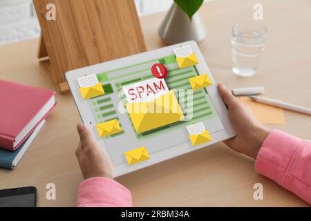 Messaggio di avviso spam, immagini delle buste che fuoriescono dal display del dispositivo. Donna che usa un software di posta elettronica su un tablet al tavolo, primo piano Foto Stock