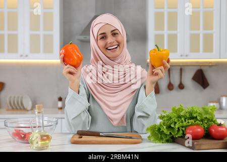 Donna musulmana che prepara una deliziosa insalata con verdure al tavolo bianco in cucina Foto Stock