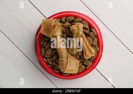 Cibo secco per cani e dolcetti (masticare le ossa) su pavimento di legno bianco, vista dall'alto Foto Stock