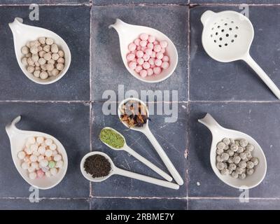 Palle di tapioca crude e crude con diversi sapori, note anche come boba in bubble tea, su sfondo grigio piastrelle. Un ingrediente per preparare il tè al latte perlato. Foto Stock