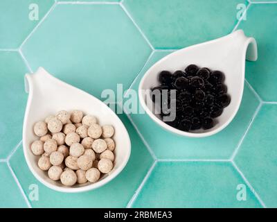 Palline di tapioca crude e cotte con diversi sapori, note anche come boba in bubble tea, su sfondo piastrellato verde. Un ingrediente per preparare il tè al latte perlato. Foto Stock