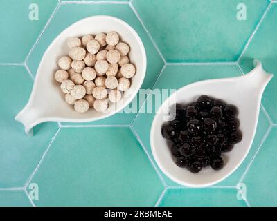 Palline di tapioca crude e cotte con diversi sapori, note anche come boba in bubble tea, su sfondo piastrellato verde. Un ingrediente per preparare il tè al latte perlato. Foto Stock