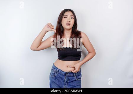 Una triste giovane donna asiatica che stringe la pelle flabby pancia grassa isolata da sfondo bianco Foto Stock