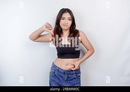 Una triste giovane donna asiatica che stringe la pelle flabby pancia grassa isolata da sfondo bianco Foto Stock