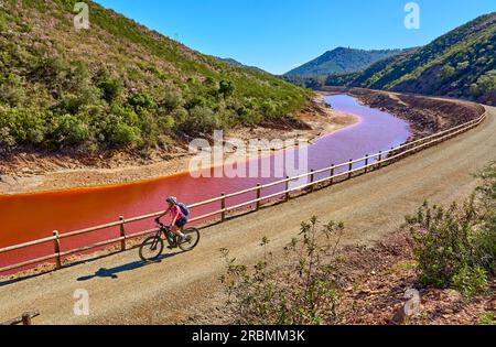 Una donna simpatica in bici elettrica in un tour in bicicletta lungo il fiume Rio Tinto con le sue acque rosse naturali in Andalusia, Spagna Foto Stock