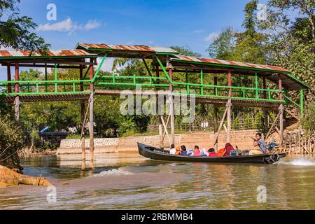 Una tradizionale barca a coda lunga su un canale nel lago Inle per trasportare le persone sotto una passerella di legno, Myanmar, Asia Foto Stock