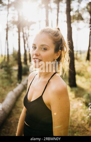 Ritratto di una giovane runner donna che si ferma per riposarsi. Donna in forma che si prende una pausa dall'allenamento all'aperto in una foresta. Foto Stock