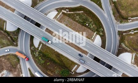 Volo aereo con droni dall'alto di automobili e traffico che viaggia in autostrada circondato da prati verdi e alberi Foto Stock