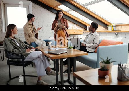 Gruppo di giovani professionisti interculturali in abbigliamento casual che discutono di punti di lavoro e di nuove idee durante il brainstorming alla riunione di avvio Foto Stock