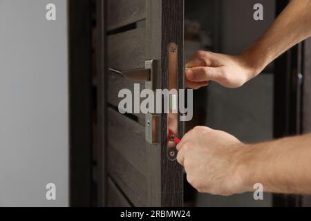 Lavoratore con cacciavite che ripara la serratura della porta in interni, primo piano Foto Stock