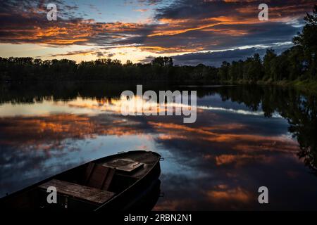 Un lago al tramonto, una barca di fronte. Nuvole arancioni nel cielo, che si riflettono nel lago. Regione Reno-Neckar, Germania. Foto Stock