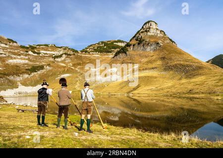 Tre musicisti austriaci di alphorn di nome "Klangholz" suonano l'alphorn al lago Augstsee sul monte Loser in Austria. Foto Stock