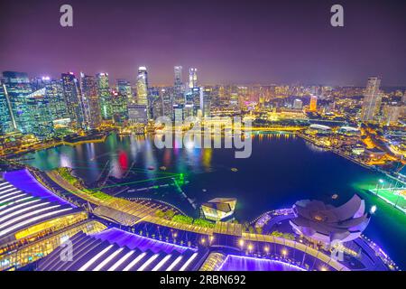 Vista aerea di Singapore Marina Bay con i grattacieli del quartiere finanziario illuminati di notte che si riflettono sul porto. Sul tetto sopra lo skyline di Singapore Foto Stock