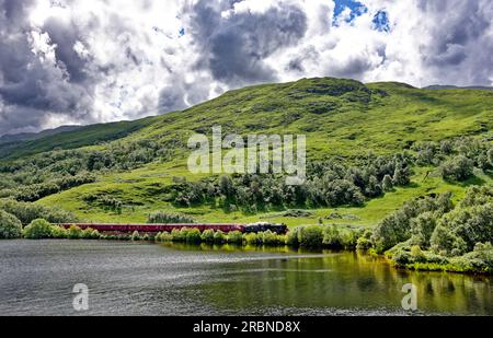 Jacobite Steam Train sul tracciato accanto a Loch Eilt vicino alla tomba di Silente Lochailort in Scozia Foto Stock