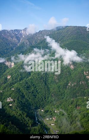 La strada Provinciale SP169 si snoda lungo il fiume Germanasca, adagiata ai piedi di lussureggianti montagne verdi, in primavera nel Piemonte Foto Stock