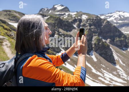 Grande ritratto di un uomo dai capelli grigi che fotografa un paesaggio montano nelle Alpi austriache Foto Stock