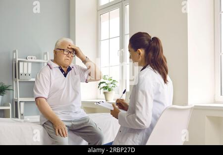 Paziente maschile anziano che soffre di mal di testa e che dice al suo medico del dolore Foto Stock