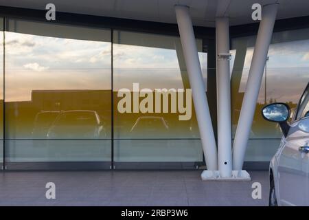 Un'auto parcheggiata di fronte a un edificio moderno con riflessi di altre auto Foto Stock