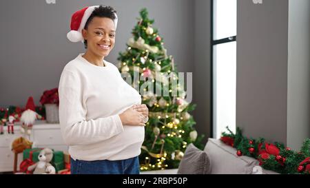 Giovane donna incinta che tocca la pancia per festeggiare il natale a casa Foto Stock
