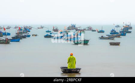 Un pescatore vietnamita sta sotto la pioggia mentre guida il suo coracle verso il suo peschereccio a Danang, in Vietnam. Foto Stock