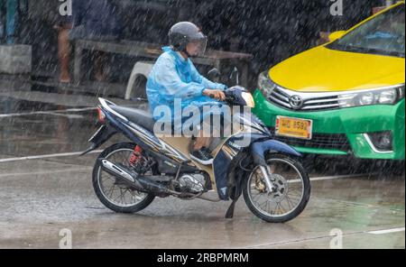 SAMUT PRAKAN, THAILANDIA, 10 MAGGIO 2023, Un motociclista con un impermeabile corre sotto una pioggia intensa Foto Stock