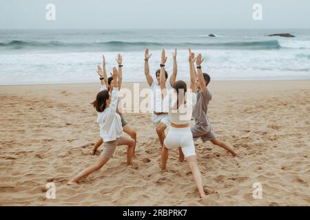 Gruppo di giovani uomini e donne in abbigliamento sportivo che fanno yoga sulla riva dell'oceano, in piedi su tappetini in cerchio, esercitano l'asana Foto Stock