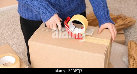 Donna che confeziona scatola di cartone con dispenser di nastro adesivo Foto Stock
