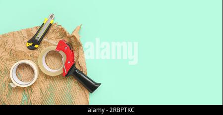 Rotoli di nastro adesivo, dispenser, coltello multiuso e carta da imballaggio su sfondo turchese con spazio per testo Foto Stock