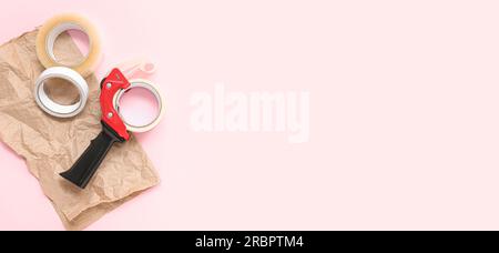 Rotoli di nastro adesivo, dispenser e carta da imballaggio su sfondo rosa con spazio per testo Foto Stock
