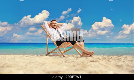 Rilassato uomo d'affari su una sdraio con un computer portatile seduto in riva al mare Foto Stock