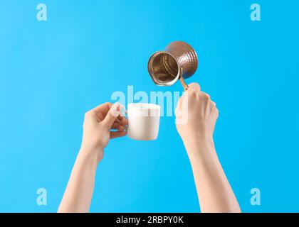 Mani femminili che tengono cezve e tazza di caffè su sfondo blu Foto Stock