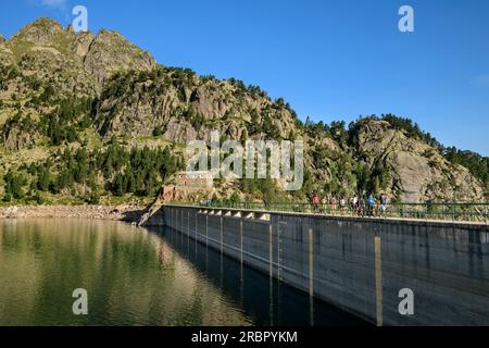 Diverse persone che camminano sopra la diga presso il lago Lac Major de Colomers, il Parco Nazionale Aigüestortes i Estany de Sant Maurici, Catalogna, Pirenei, Spagna Foto Stock