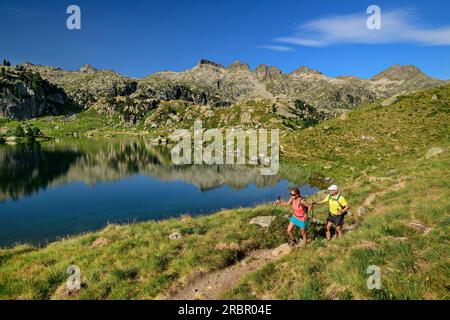 Uomo e donna passeggia per il lago di montagna Estanh Plan, Circ de Colomers, Aigüestortes i Estany de Sant Maurici National Park, Catalogna, Pirenei, Spagna Foto Stock