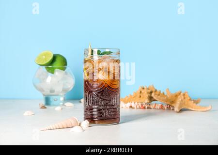 Bicchiere di freddo Cuba Libre cocktail, conchiglie e stelle di pesca su un tavolo bianco Foto Stock