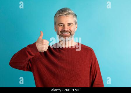 Sorridente uomo maturo dai capelli grigi che mostra il pollice in alto Foto Stock