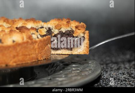 una torta appena sfornata è disposta su un piatto di torta. Un pezzo di torta viene estratto con una spatola per torta. Lo sfondo è scuro. Foto Stock