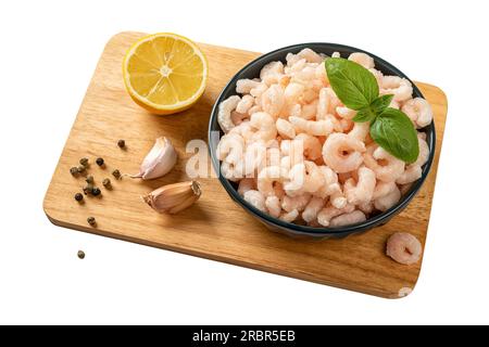 Gamberetti congelati in un recipiente sopra il tagliere. Code di gamberi pelati bolliti, limone, aglio e pepe isolati su sfondo bianco. Cibo a basso contenuto calorico Foto Stock